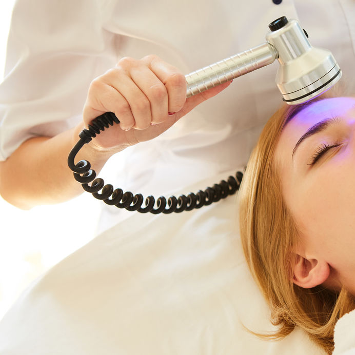 Young healthy woman with good skin doing cosmetic procedures in spa clinic. Light treatment